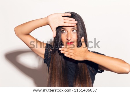 Young adult woman framing her face with her hands, making funny faces. In studio over a white background.