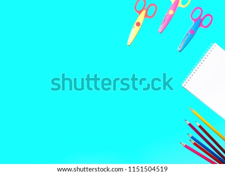 flat lay picture of colored pencils, notepad and scissors lined on a flat surface of an isolated blue background