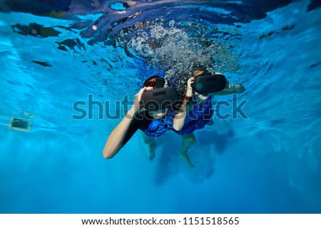 A woman and a child swim and play with virtual reality glasses on the head under the water in the pool. Shooting underwater. The horizontal orientation of the image.