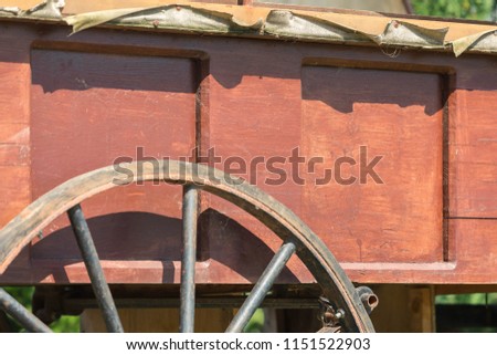 Close up of the old wooden cart with a wooden wheel in a rusty metal rim. Cart board colored red paint