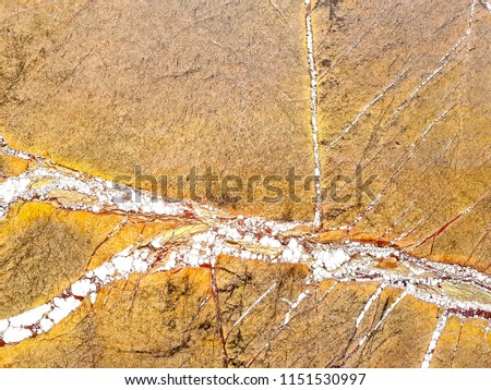 A close up of a granite block with a cracked pattern in yellow , orange , white and reddish colors.