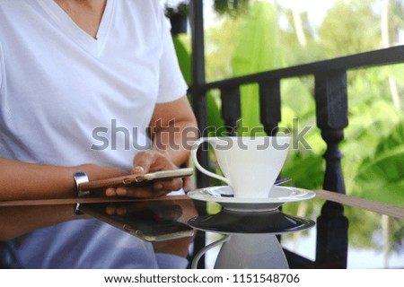 Hot coffee in white glass, served on a table in front of a woman watching a text message on a mobile phone. At the garden terrace Royalty-Free Stock Photo #1151548706