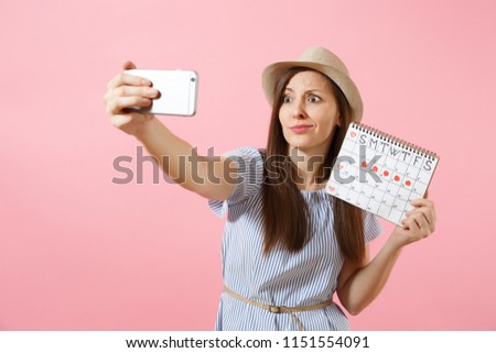 Excited woman in blue dress doing selfie on mobile phone, holding periods calendar for checking menstruation days isolated on pink background. Medical, healthcare, gynecological concept. Copy space