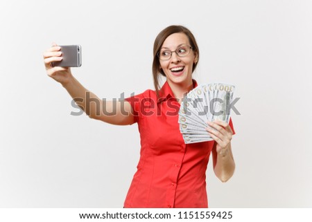 Excited business woman in red shirt doing taking selfie shot on mobile phone with bundle lots of dollars, cash money isolated on white background. Education teaching in high school university concept