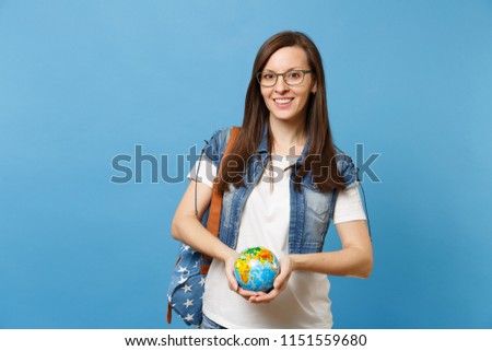Young attractive woman student in denim clothes glasses with backpack holding world globe isolated on blue background. Education in high school. Save planet. Ecology environment protection concept