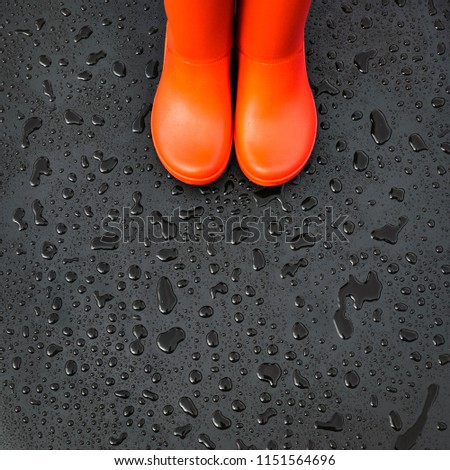 The edges of the orange rain boots are on a wet wet surface covered with raindrops. Top view, copy space.