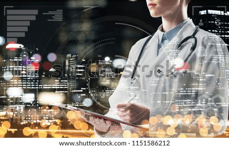 Cropped image of young medical industry employee writing in notebook while standing against night city view and media interface on background. Confident female doctor. Double exposure