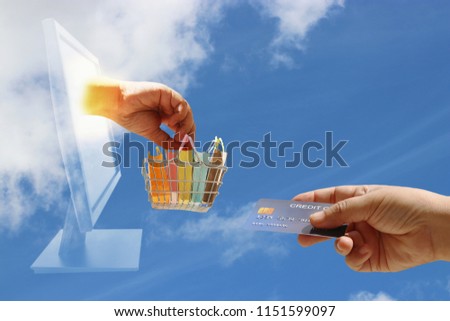 Hand holding basket of color shopping paper bags came out from screen and another hand holding mock up of credit card on cloud. Online shopping and e-commerce with cloud computing technology concept.