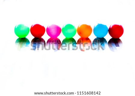 Small balls of blue, green, orange, pink, red, blue, with white background and floor reflection, colorful balloons.
