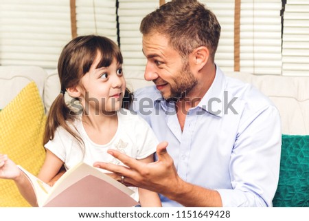 Father with little daughter having fun and read the book together on the sofa at home.Little girl and daddy enjoying with story book.Love of family and concept