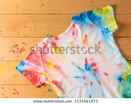 T-shirt painted in the style of tie dye on a wooden desktop. FLat lay. The view from the top.