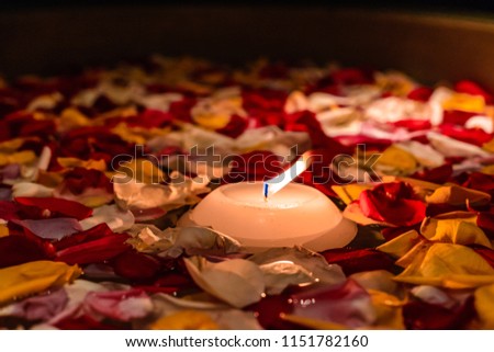 A single floating candle in a pool of dimly lit rose petals on the surface of water.