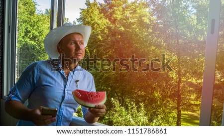 Young Handsome  male caucasian hand gestures with pointing finger showing something. Man with smarphone and cowboy hat at the window . Toned vintage picture with forest. Copy space and text box
