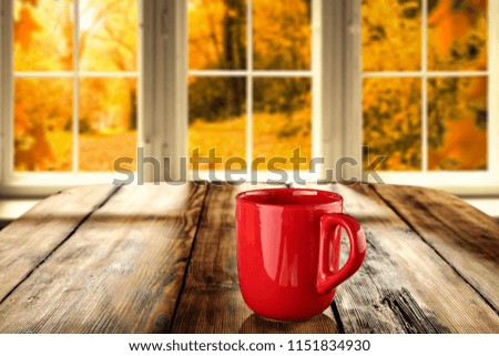 Mug on desk and window with autumn landscape 