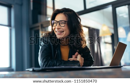 Woman sitting at the desk with laptop looking away and smiling. Asian woman in casuals at office. Royalty-Free Stock Photo #1151850470