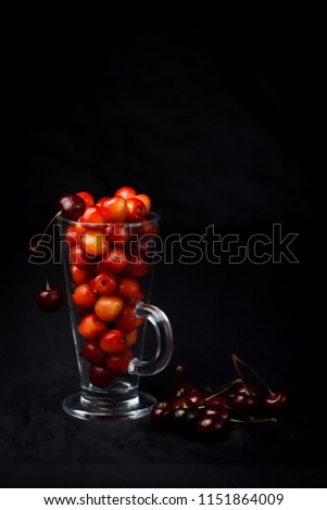 berries of red cherries in a glass on a black background. cherries and cherries on the table. atmospheric, beautiful, colorful photo of the summer season