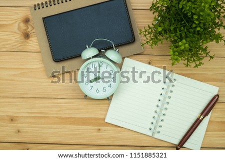 Office supplies or office work essential tools items on wooden desk in workplace, pen with notebook and alarm clock with copy space, top view