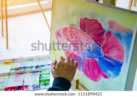 Artist drawing, watercolor painting to goldfish from a real model with hand, brush and palette in the gallery. Picture of Ornamental fish from imagine.