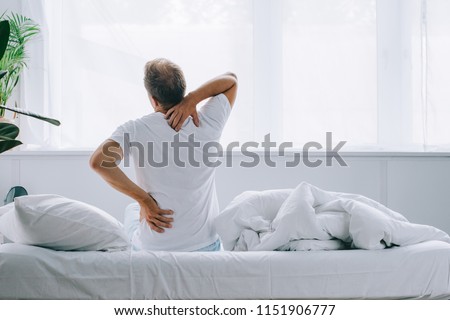 back view of man sitting on bed and suffering from back pain Royalty-Free Stock Photo #1151906777