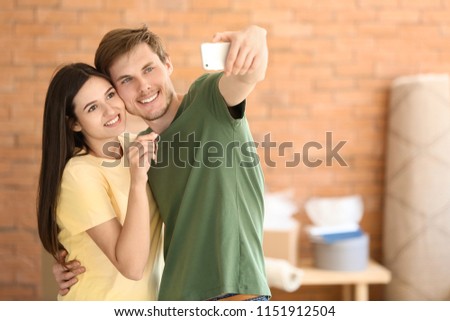 Young happy couple taking selfie with key of their new house indoors