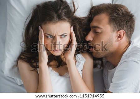 top view of young woman with headache looking at husband snoring in bed Royalty-Free Stock Photo #1151914955