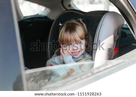 Little girl with blue eyes wearing a seat belt in a child seat in the car