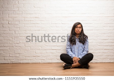 Young indian woman sit against a brick wall worried and overwhelmed, forgetful, realize something, expression of shock at having made a mistake