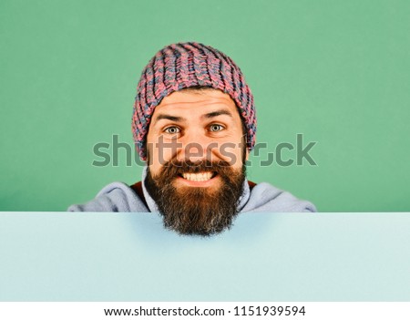 Autumn and cold weather concept. October and November sale idea. Hipster with beard and smiling face wears warm clothes. Man in warm hat on green and cyan background, copy space.
