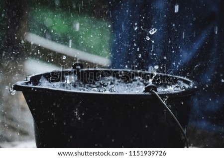 Rainy weather on the terrace in summer. The rain falls into the bucket and creates splashes.