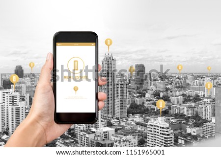 Hand holding smartphone with application to find  real estate on screen and buildings in the city as background