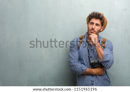 Young handsome traveler man wearing a straw hat, a backpack and a photo camera thinking and looking up, confused about an idea, would be trying to find a solution