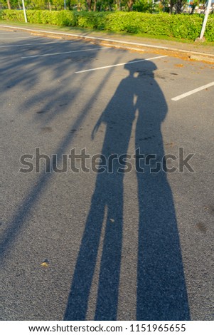 Abstract shadow shape of two persons under the same umbrella projection on empty road or car parking lot outdoor in evening sunset time, a couple of lovers or romantic travel concept