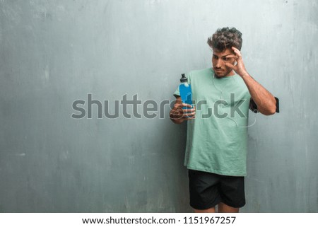 Young fitness man against a grunge wall surprised and shocked, looking with wide eyes, excited by an offer or by a new job, win concept. Holding a blue energy drink.
