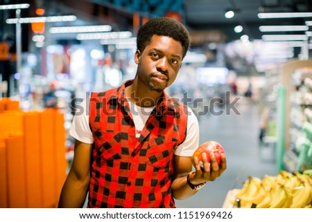 Young african man buying vegetables and fruits in grocery section at supermarket. Black man choose vegetables and fruits in the supermarket while holding grocery basket. 