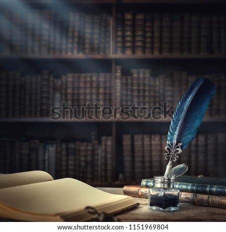 Old quill pen, books and vintage inkwell on wooden desk in the old office against the background of the bookcase and the rays of light. Conceptual background on history, education, literature topics. Royalty-Free Stock Photo #1151969804