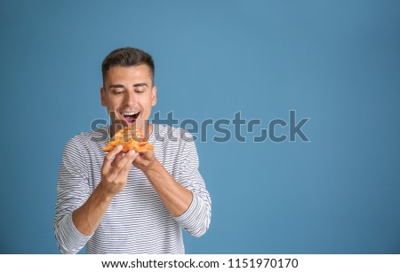 Handsome young man with delicious pizza on color background