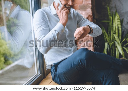cropped image of businessman talking on smartphone and looking at wristwatch at home