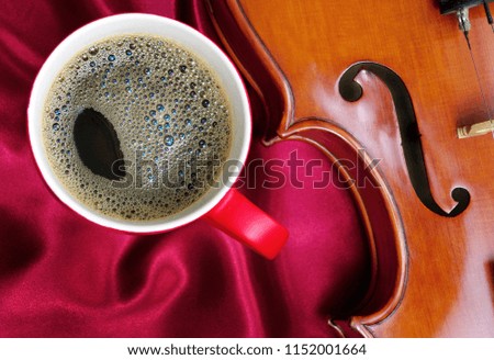 cup of coffee and a violin on a red silk background. close up. top view.
