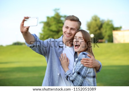 Young couple taking selfie in park on sunny day