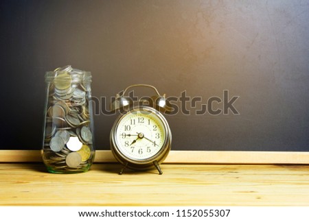 Silver coins in a glass jar with a retro alarm clock. Concept of saving money for the future.
