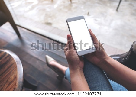 Mockup image of woman's hands holding white mobile phone with blank desktop screen while sitting in cafe