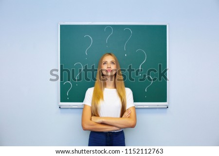 Beautiful female student with lots of question marks questioning expression and question marks above her head. Student thinking with question marks on blackboard.