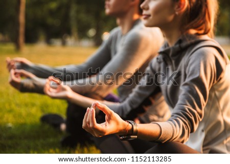 Image of concentrated fitness sport loving couple friends in park outdoors make meditate exercises.