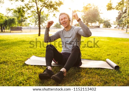 Picture of handsome fitness sportsman in park outdoors listening music with headphones.