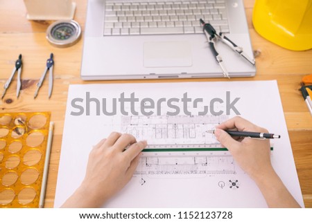 Close-up Architect or engineer hands working on blueprint plans  with  a pencil,  a ruler, calculator, smartphone, laptop and engineering tools. Architect or engineer working on blueprint in office. 