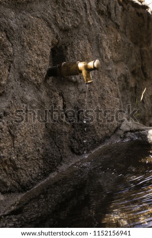 Stone fountain with an iron spout with water running
