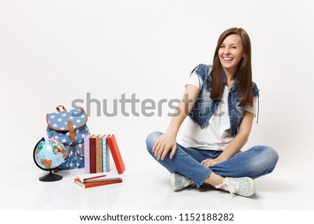 Full length portrait of young casual laughing woman student in denim clothes sitting near globe backpack school books isolated on white background. Education in high school university college concept