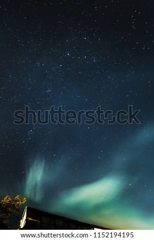 Astrophotography - the northern lights and stars above the roof of the house