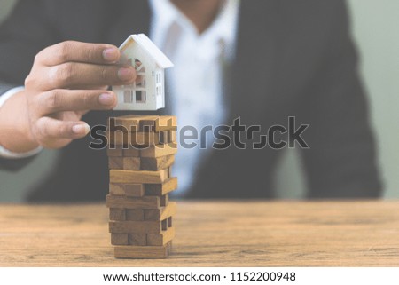 Businessman hand holding model white house on wood block. Investment risk and uncertainty in the real estate housing market. Property investment and house mortgage financial concept. with copy space
