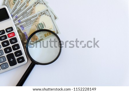 Business and finance theme. Copy space of text or logo. Calculator,bank notes or dollar bill and magnifying glass isolated on white background.